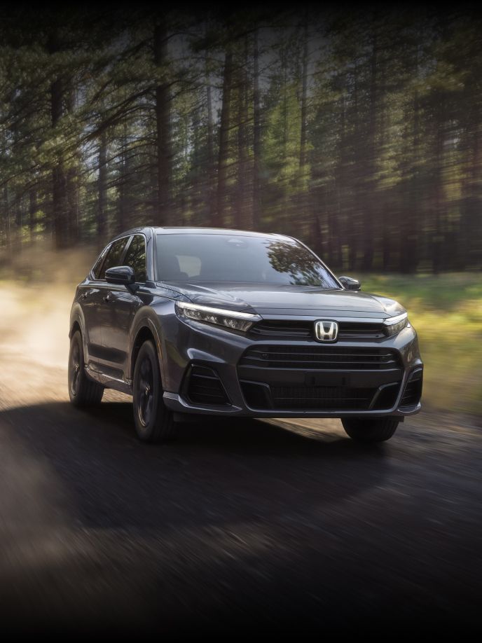 Front passenger action shot of 2025 CR-V e:FCEV in Meteorite Gray Metallic driving off-road on along a tree lined path.
