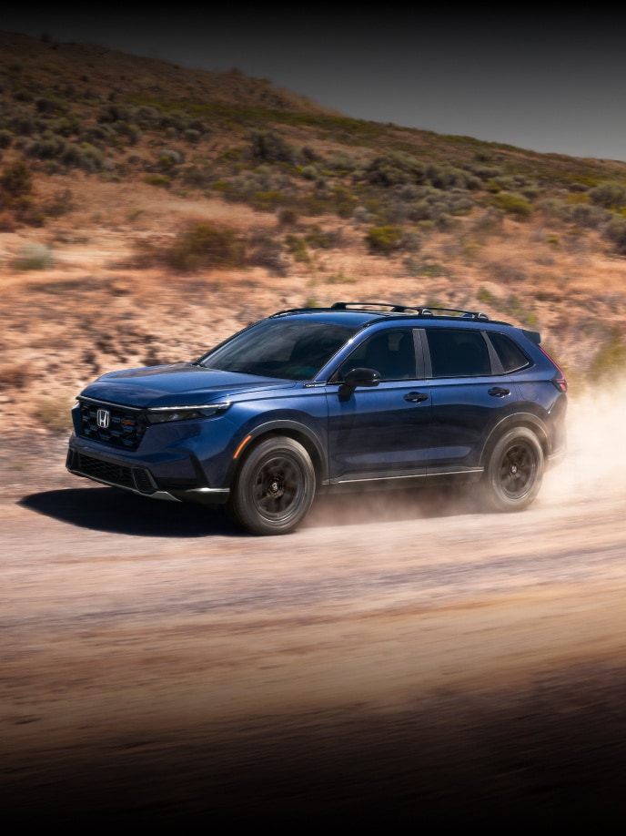 2027 Honda CR-V TrailSport Hybrid in Canyon River Blue Metallic profile driving on a dirt road (Compact Crossover SUV).