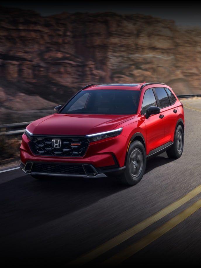 2027 Honda CR-V TrailSport Hybrid in Radiant Red Metallic front driving on a winding canyon road (Compact Crossover SUV).