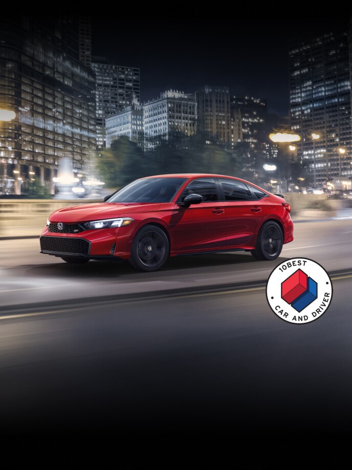 2026 Honda Civic Si Sedan in Rallye Red front 3/4 driving in a city at night with overlapping Car and Driver 10Best logo (Sporty Compact Sedan).