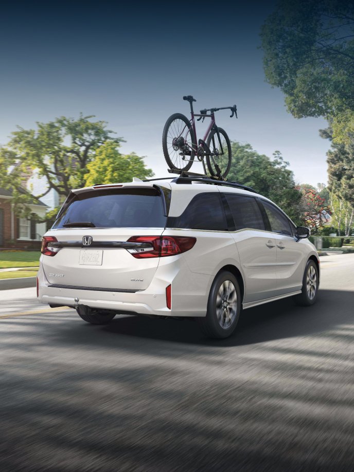2027 Honda Odyssey Elite in Platinum White Pearl back driving through a sunny residential neighborhood (Minivan).