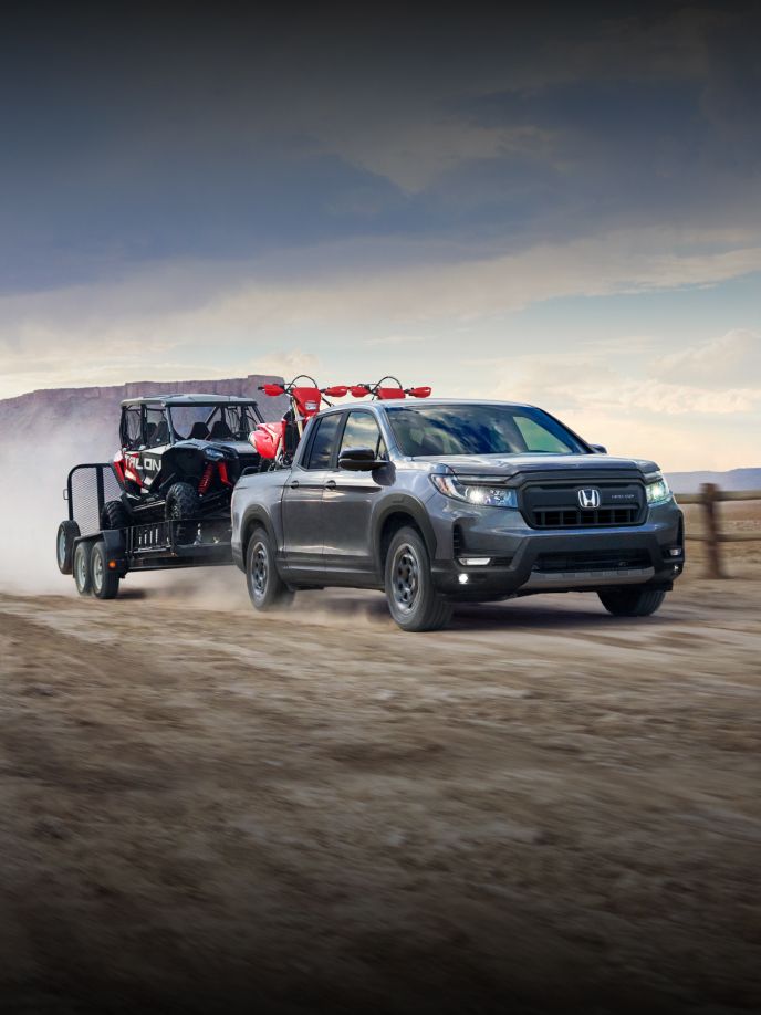2024 Honda Ridgeline TrailSport in Modern Steel Metallic drives through a dirt field towing a trailer