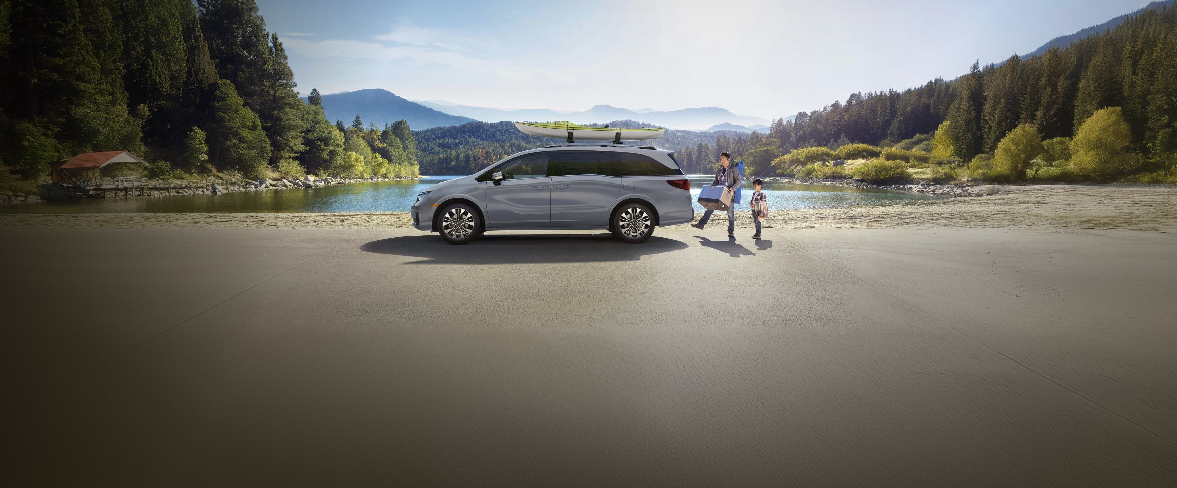 2026 Honda Odyssey Elite in Sonic Gray Pearl parked at lake with hills and greenery in background. 
