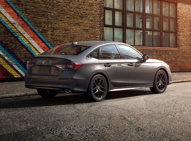 2026 Honda Civic Sedan Sport in Meteorite Gray Metallic rear three-quarter view parked on a city street (Compact Sedan)