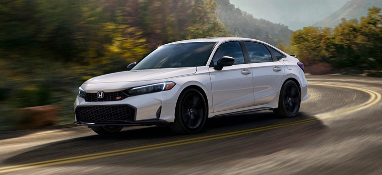 2026 Honda Civic Si Sedan in Platinum White Pearl front 3/4 driving on a winding road (Sporty Compact Sedan).
